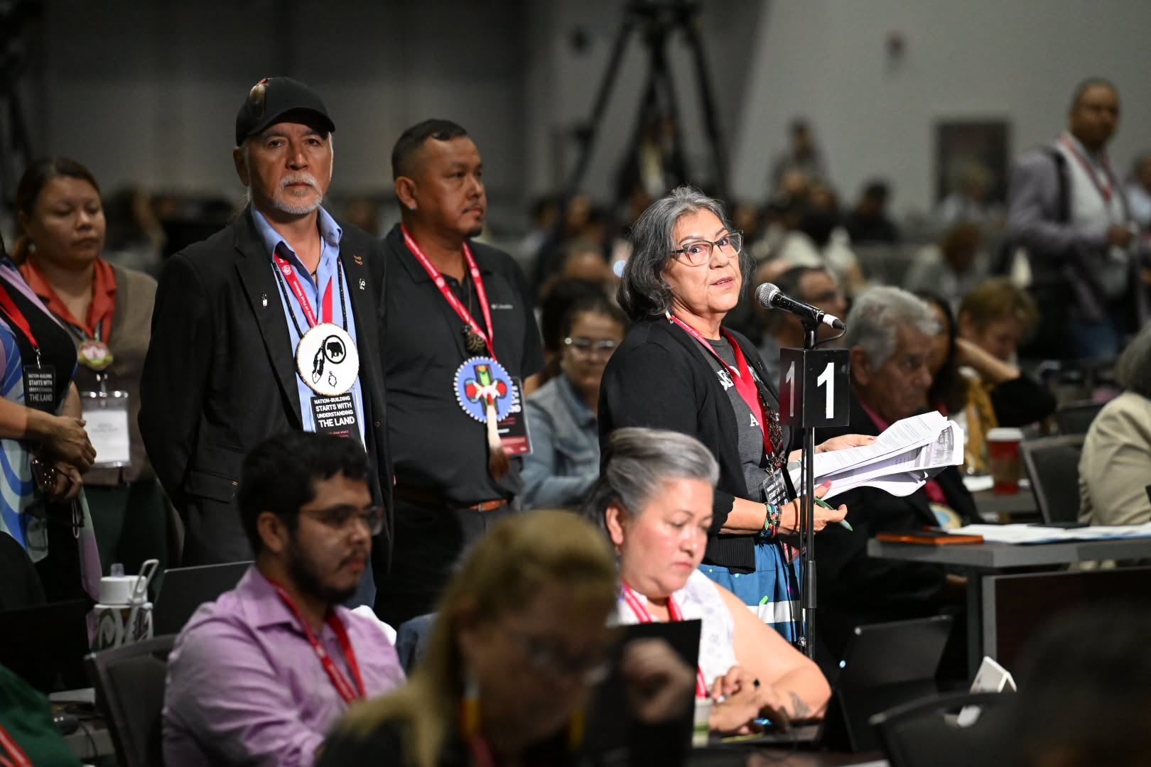 Chief Veronica Smith standing at the microphone mid-speech at AFN. Chiefs are shown in line behind her.